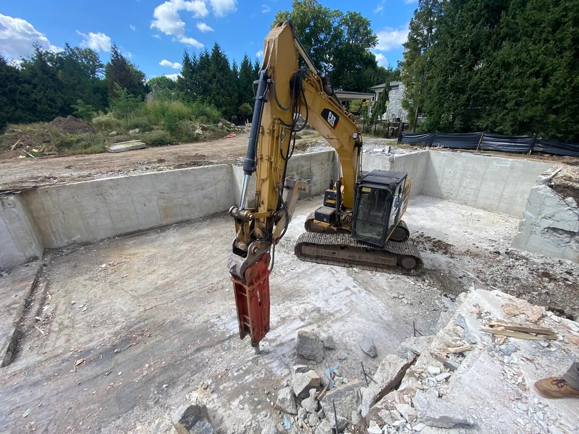 Excavator with breaker demolishing pool foundation